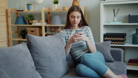 Schöne-junge-Frau-berühren-Smartphone-Bildschirm-auf-couch-im-Haus