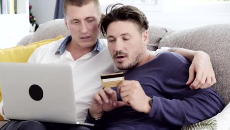 Gay-couple-relaxing-on-couch-using-laptop-computer.-Try-to-see-credit-card-number.