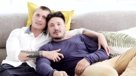 Gay-couple-relaxing-on-couch.-Holding-television-remote.