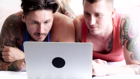 Gay-couple-in-bed-using-laptop-computer.-Laughing.