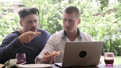 Gay-couple-having-pizza-for-lunch.-Browsing-and-eating-pizza.