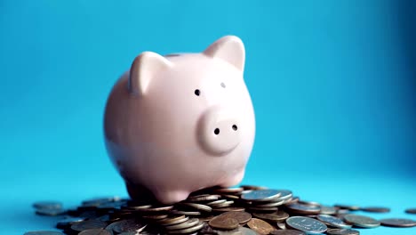 Man-putting-coins-in-piggy-bank-of-pig-shape-in-pile-of-coins,-hand-closeup