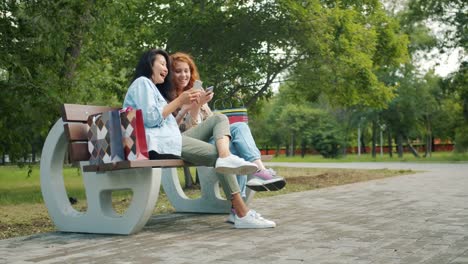 Beautiful-girls-teenagers-using-smartphones-relaxing-on-bench-in-park-laughing