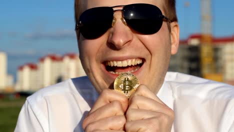 A-man-in-black-glasses-is-holding-a-bitcoin-in-his-hands-and-laughing,-happy,-close-up