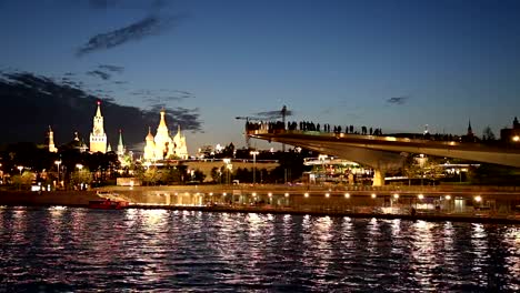 Floating-bridge-of-Zaryadye-park-on-Moskvoretskaya-Embankment-of-Moskva-River-(and-tourist-pleasure-boat)-at-Night.-Moscow,-Russia.