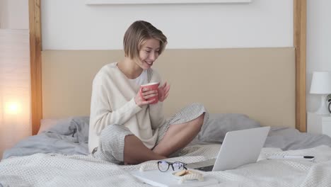 Mujer-feliz-haciendo-videollamada-usando-computadora-portátil-en-la-cama