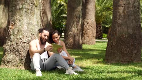 Man-and-woman-relaxing-with-digital-tablet-in-park-after-sports-training