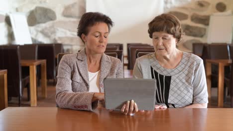 Feliz-madre-e-hija-usando-tableta-digital-juntos-en-la-cafetería