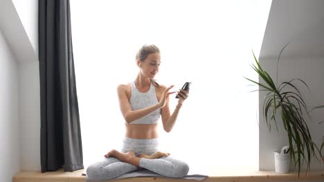 Mujer-sentada-en-el-alféizar-de-la-ventana-viendo-videos-en-teléfonos-inteligentes-y-auriculares