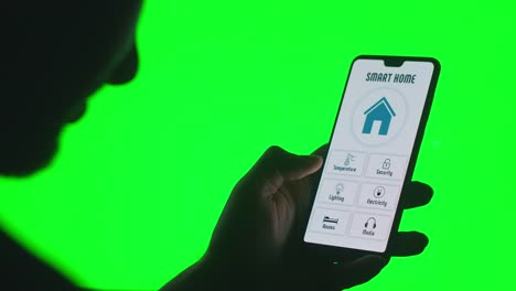 Die-Hand-steuert-die-Smart-Home-App-mit-einem-Smartphone-auf-grünem-Chromakey-Hintergrund