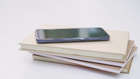 Female-hand-reaching-to-pick-up-her-cellphone-from-top-of-the-books