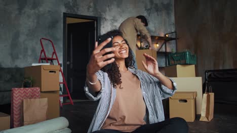 Pareja-en-movimiento-en-nuevo-apartamento.-Hombre-desempaquetando-plantas.-Mujer-sonriendo,-saludando-y-grabando-video-para-su-blog-usando-el-teléfono-inteligente.-Cámara-lenta