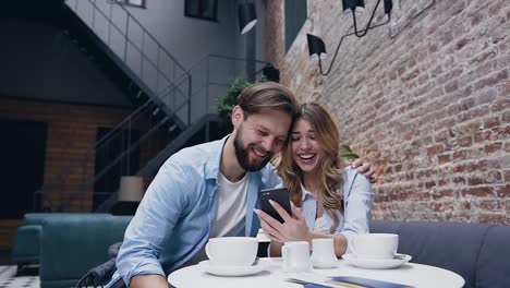 Schöne-fröhliche-Bart-Mann-aufrichtig-lachen-mit-seiner-hübschen-blonden-Freundin-während-Revision-lustige-Video-auf-ihrem-Handy