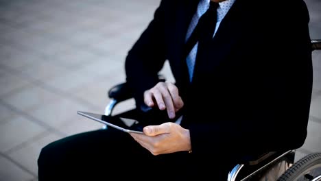 Handicapped-businessman-sitting-in-wheelchair-outdoor-and-work-with-digital-pad