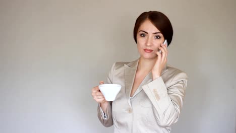 Beautiful-young-businesswoman-looks-at-the-phone-screen-and-plays-downloaded-application-on-a-smart-phone.-Elegant-woman-communicate-in-social-networks-and-drinks-coffee