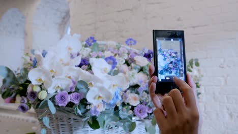 Woman-taking-photo-of-large-floral-basket-with-flowers-with-smartphone.