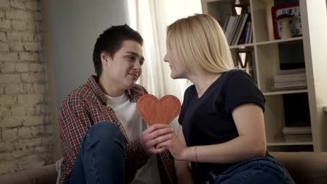 Two-young-lesbians-cute-look-at-each-other,-holding-a-heart-sign-in-their-hand.-60-fps