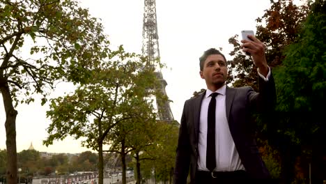 Hombre-atractivo-en-un-traje-lleva-un-selfie-en-un-teléfono-inteligente-junto-a-la-Torre-Eiffel