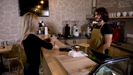 Alegre-trabajador-atender-a-clientes-mujer-que-usan-su-smartphone-app-y-bitcoin-moneda-crypto-para-pagar-en-una-tienda-de-café