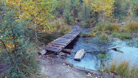 Cruce-pequeño-Malecón-de-madera-puente-sobre-Arroyo-de-bosque-cerca-del-lago-azul-Geyser-en-montañas-de-Altai-en-día-de-lluvia