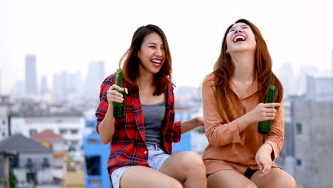 Young-asian-woman-lesbian-couple-clinking-bottles-of-beer-party-on-rooftop.