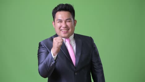 Young-handsome-overweight-Asian-businessman-against-green-background