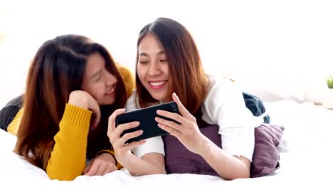 Joven-pareja-de-lesbianas-asiáticas-selfie-en-smartphone-en-habitación-con-cama-en-casa.