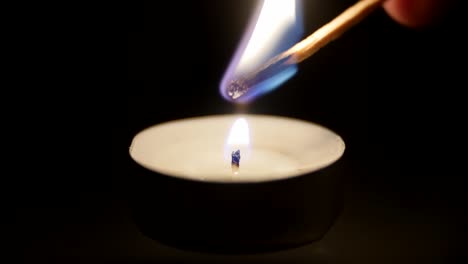 Close-up-of-a-match-lighting-a-candle-against-a-black-background