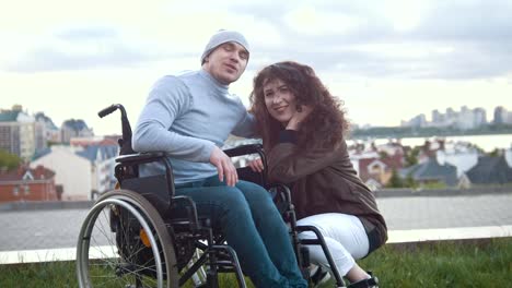 Portrait-of-a-happy-disabled-man-in-a-wheelchair-embraces-with-young-woman-outdoors