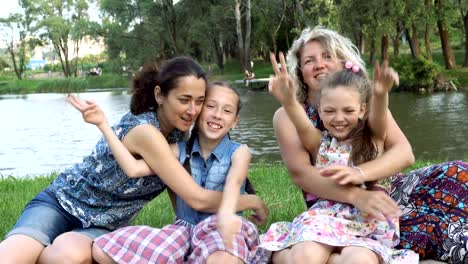 Two-happy-mothers-with-two-small-children-play-and-have-fun-sitting-in-the-Park-on-the-lawn-at-sunset.-Close-up.-4K,-29.97-fps.