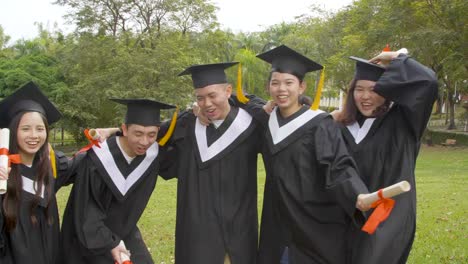 happy--students-in-graduation-gowns-holding-diplomas-on-university-campus