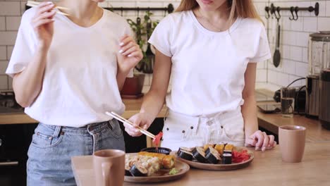 Two-funny-young-lesbians-eat-sushi-rolls-at-home.