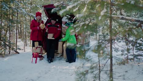 Happy-family-looking-New-Year-gift-in-car-trunk-in-winter-forest.-Mom,-dad,-son-and-daughter-in-red-Christmas-hat-having-fun-together-dog-in-snowy-woodland-at-winter-holiday.