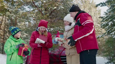 Glückliche-Familie-überprüfen-Neujahrsgeschenke-im-verschneiten-Wald-bei-Winterspaziergang.-Fröhliche-Tochter-Öffnen-Box-mit-Weihnachtsgeschenk-auf-Waldspaziergang.-Frohes-Neues-Jahr-und-Weihnachten.