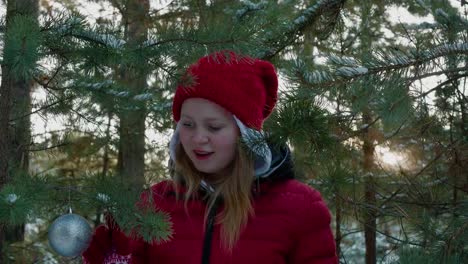 Glückliches-Mädchen-spielen-mit-verschneiten-Kiefer-Zweig-im-Winterwald.-Junge-Frau-berühren-Nadelbaum-Zweig-mit-Weihnachtskugel.-Teenager-Mädchen-im-Neujahr-Wald.