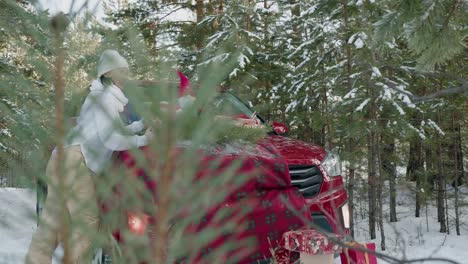 Beautiful-woman-holding-Christmas-present-on-red-car-background-in-snowy-forest.-Adult-woman-with-New-Year-gift-near-red-car-in-snowy-woodland-at-winter-holiday.