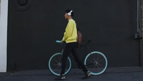 Transgénero-adulto-caminando-con-una-bicicleta-y-usando-auriculares