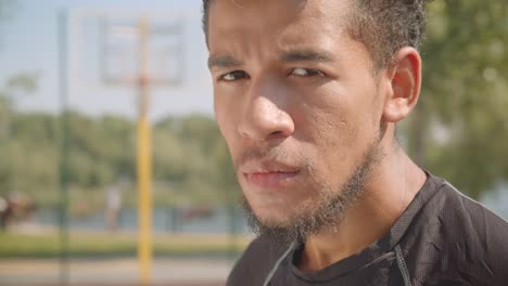 Retrato-de-primer-plano-de-joven-guapo-jugador-de-baloncesto-masculino-afroamericano-mirando-a-la-cámara-estar-cansado-sentado-al-aire-libre