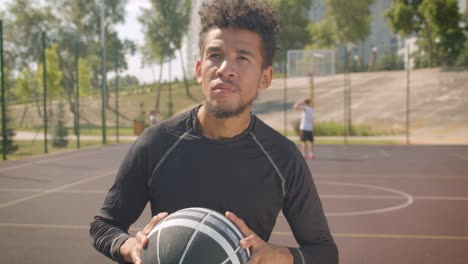 Retrato-de-primer-plano-de-joven-guapo-jugador-de-baloncesto-masculino-afroamericano-lanzando-una-pelota-en-un-aro-al-aire-libre