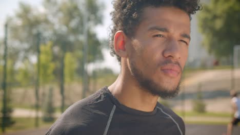 Retrato-de-primer-plano-del-joven-guapo-jugador-de-baloncesto-afroamericano-masculino-girando-y-mirando-la-cámara-al-aire-libre