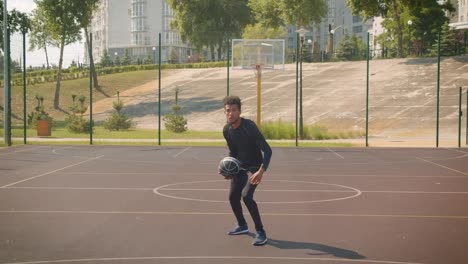 Retrato-de-primer-plano-de-joven-atractivo-jugador-de-baloncesto-afroamericano-masculino-lanzando-una-pelota-en-un-aro-al-aire-libre-en-la-cancha