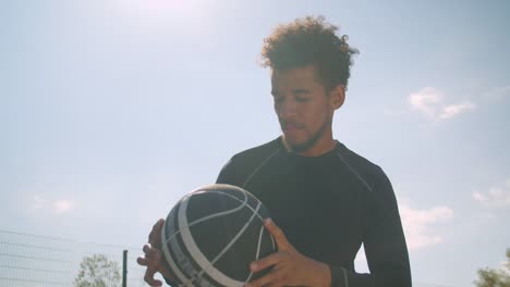 Retrato-de-primer-plano-de-joven-experto-jugador-de-baloncesto-afroamericano-masculino-lanzando-una-pelota-en-un-aro-al-aire-libre