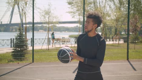 Retrato-de-vista-lateral-de-joven-guapo-jugador-de-baloncesto-masculino-afroamericano-lanzando-una-pelota-en-un-aro-al-aire-libre