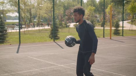 Retrato-de-primer-plano-del-joven-guapo-jugador-de-baloncesto-afroamericano-masculino-lanzando-una-pelota-en-un-aro-al-aire-libre-en-la-cancha