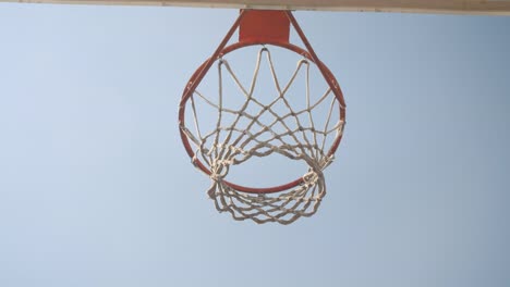 Primer-plano-abajo-vista-retrato-de-la-pelota-de-baloncesto-que-se-lanza-en-un-aro-al-aire-libre-en-la-cancha-con-el-cielo-en-el-fondo