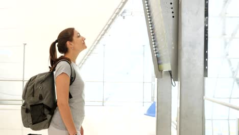 brunette-girl-with-backpack-looks-at-flight-schedule