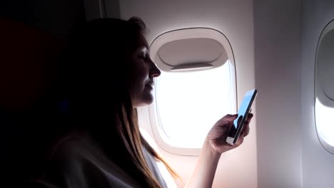 lady-in-grey-t-shirt-looks-at-phone-against-bright-porthole