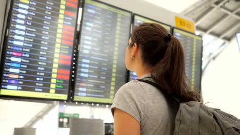 brunette-looks-at-departures-schedule-in-airport-terminal