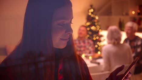 Pelirroja-adolescente-chica-usando-teléfono-inteligente.-Sonriendo.-Riendo.-Navidad-detrás-del-cristal.