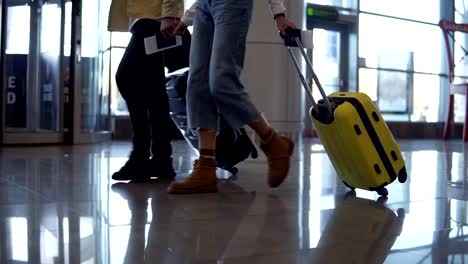 Las-imágenes-frontales-recortadas-de-un-par-de-viajeros-llevan-su-equipaje-y-se-tienen-de-la-mano.-Caminando-sobre-el-salón-de-la-terminal.-La-gente-se-prepara-para-abordar-y-salir-con-maletas-rodantes.-A-cámara-lenta.-Vista-lateral